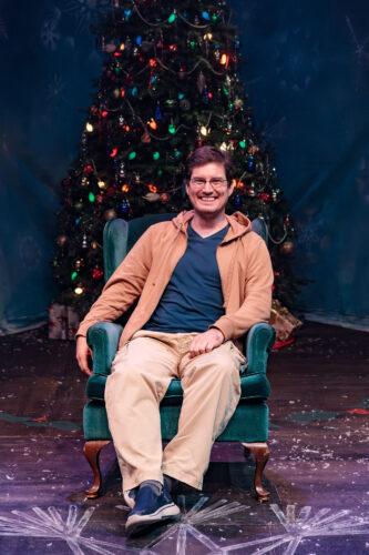 Composer Billy Thompson sits in a velvet green chair in front of a Christmas tree on the Cygnet stage.